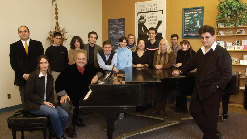 Group photo of musicians standing around a piano