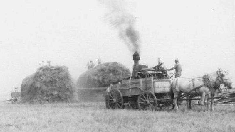 black and white photo of a farming machine and large bales of hay