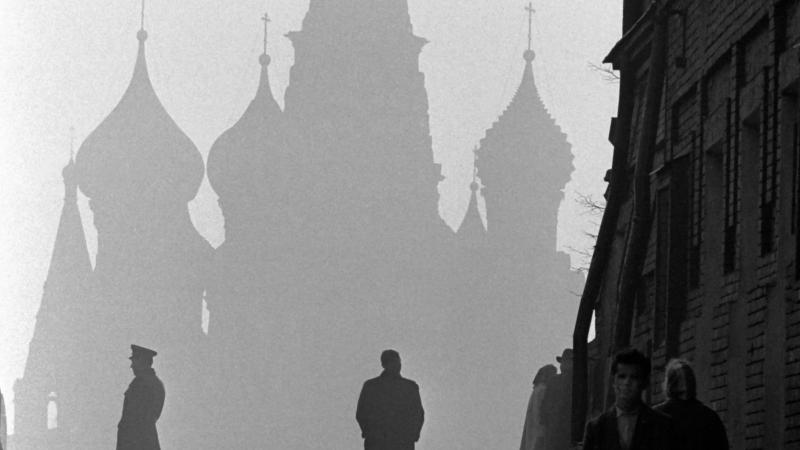 A few people walk on a wide sidewalk, with the shadow of the kremlin rising through the mist in the background