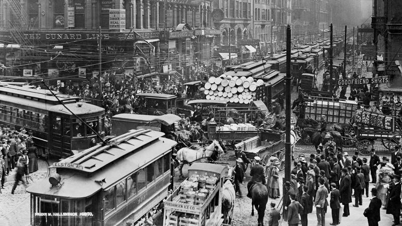 Streetcars, trucks and cars fight to cross an intersection, while crowds of pedestrians move around the gridlock