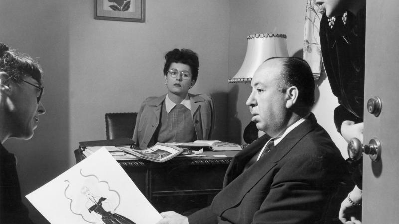 black and white photograph of man in chair in foreground, woman at desk in background
