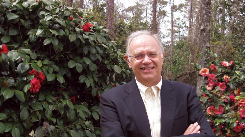 Photograph of a man in a suit standing in rose garden