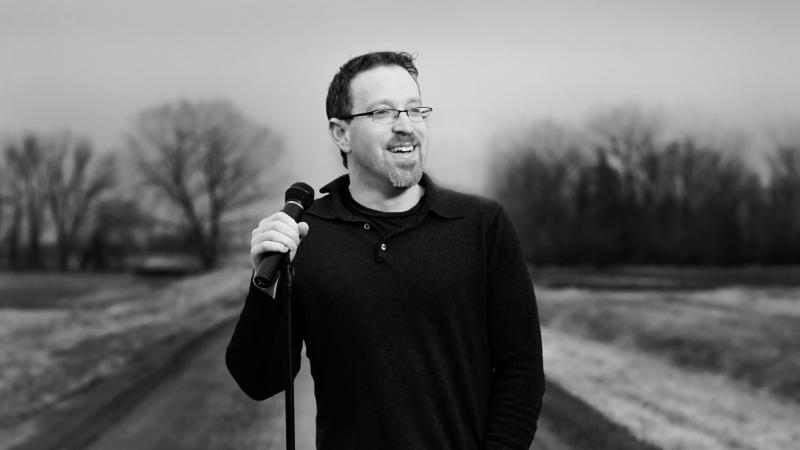 black and white photograph of a man standing in the road, holding a microphone