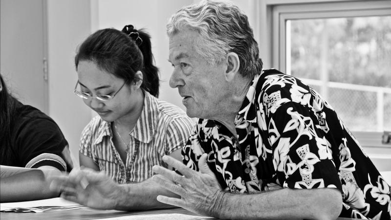 black and white photograph of a man excitedly talking at a table, a woman sits next to him