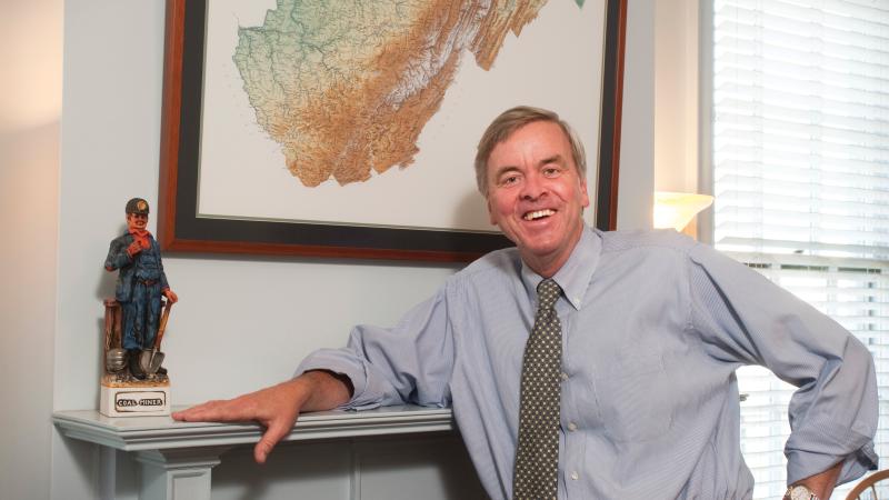 Color photo of Ken Sullivan posing for a portrait next to a fireplace hearth.