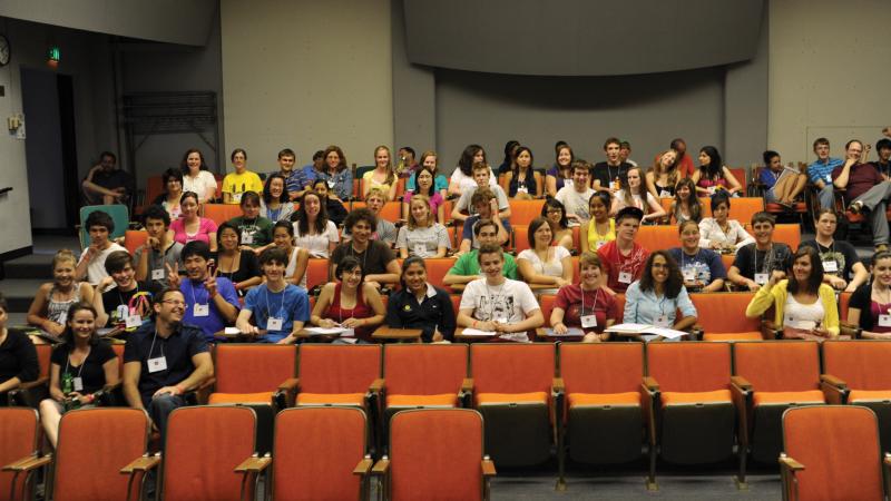 Color photo of many students sitting in an auditorium, smiling.