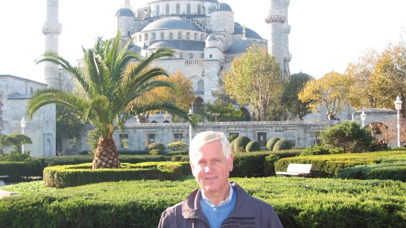 Color photo of Gale Peterson standing before a large mosque and its elaborate gardens.