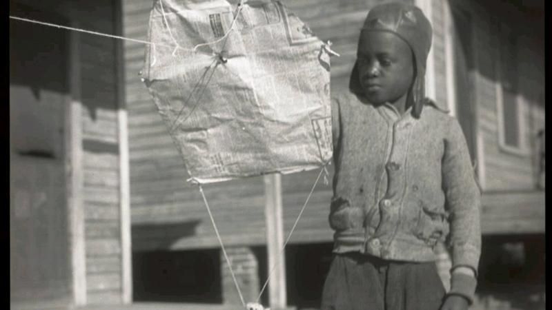 Black and white photo of an African American child playing with a kite.