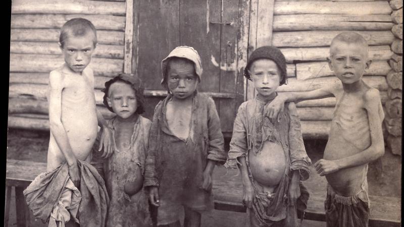 Five children, dressed in rags, stand in front of a wood doorway, stomachs bloated and ribs exposed
