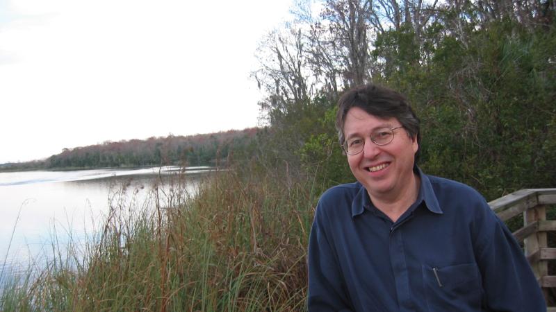 Hyde in a blue shirt, leaning on a railing overlooking a grassy pond