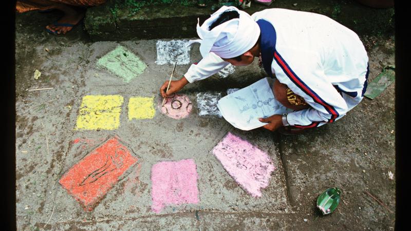 A priest kneels on the sidewalk, drawing