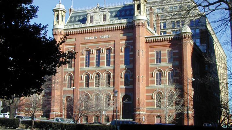 Red brick, five story building with a green tiled roof