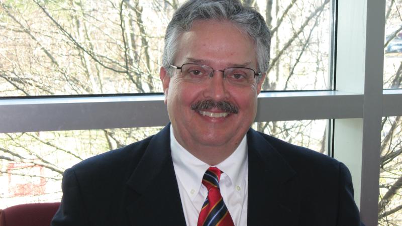 Paul Austin wearing glasses, wearing a red and blue striped tie and dark suit jacket