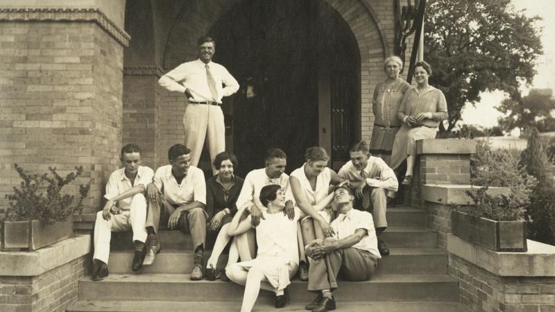 Reed Family and friends sitting on the steps to the house, with David Reed standing at the top of the stairs, hands on hips