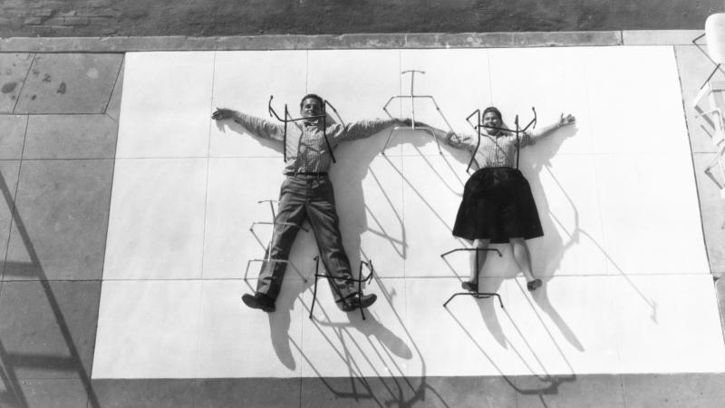 A man and a woman spread out in snow angel fashion over a concrete block, to which they are pinned by rods.