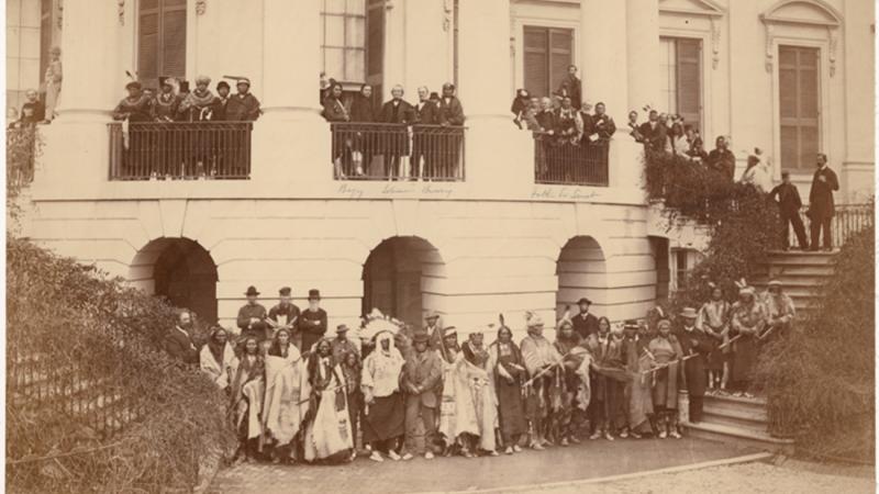 Sepia-colored photo of a large Native American delegation standing in front of the White House.
