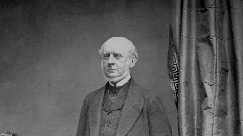 Black and white photo portrait of Charles Francis Adams standing upright in front of a curtain.