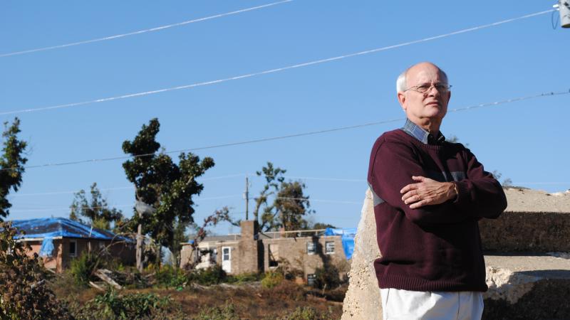 Color photo of Bob Stewart standing amid damaged houses.
