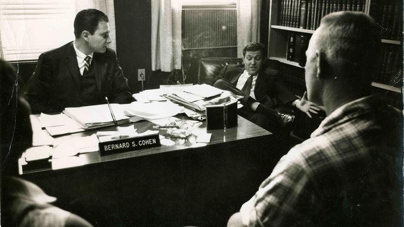 Black and white photo showing two lawyers behind a desk with the Loving couple seated in front of them.