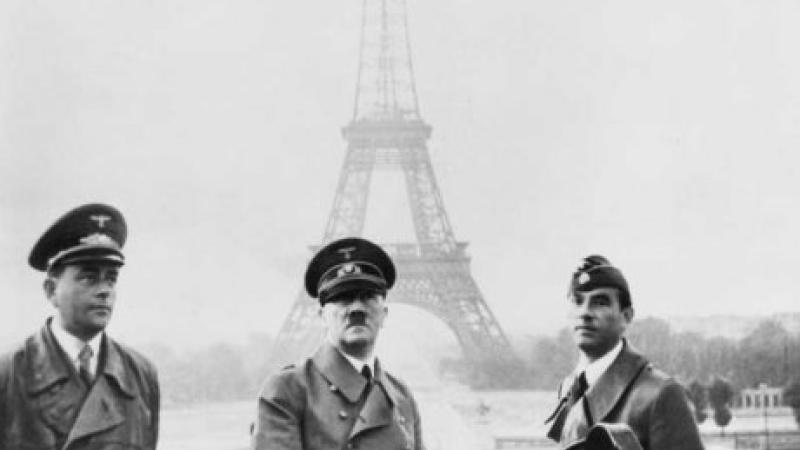 Black and white photo of three military men (including Adolf Hitler) standing in front of the Eiffel Tower.