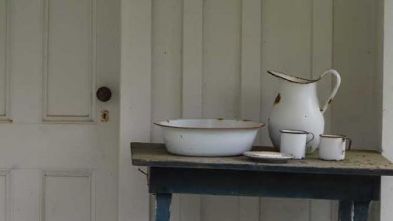 Color photo of a pitcher and two teacups on a table, with an aged wooden door in the background. 