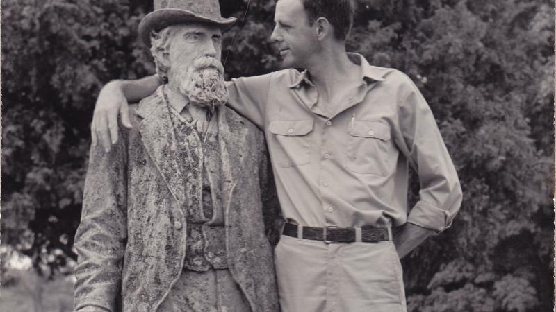 Black and white photo of Wendell Berry putting his arm around the statue of an old man.