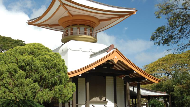 Color photo of a temple with a pagoda amid lush trees.