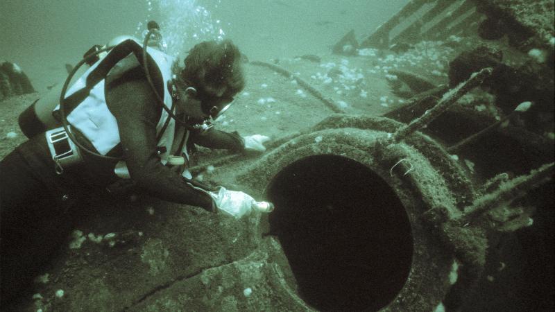 Photo of a scuba diver pointing at the torpedo loading hatch of a sunken submarine.