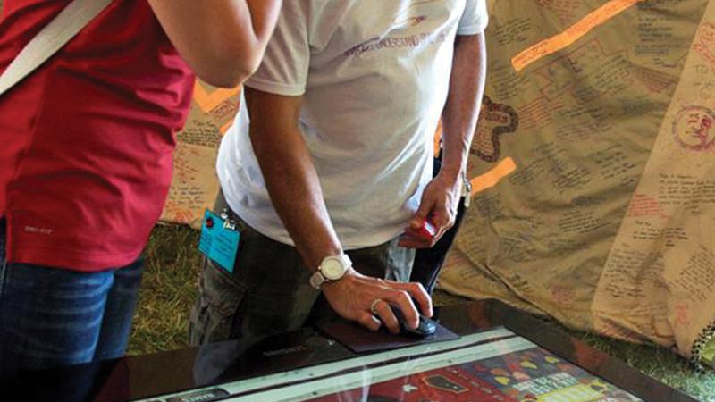 Color photo of two individuals staring down at what looks to be a sort of digital gaming table.