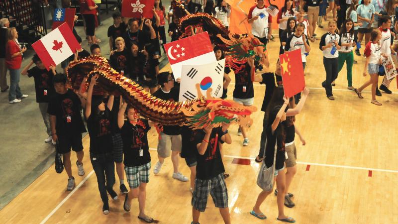 Photo of young students carrying a Chinese dragon and the flags of China, South Korea, and Canada.