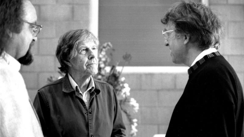 Black and white photo of John Cage meeting with another man.