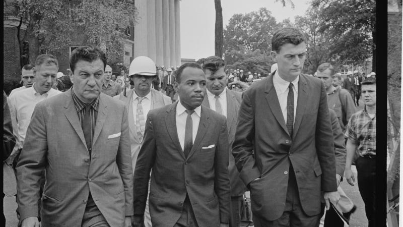 Black and white photo of bureaucrats in suits walking as an entourage.