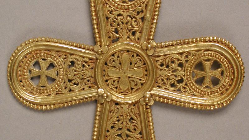 A gold pendant in the shape of a cross, with rounded edges and intricate filigree designs