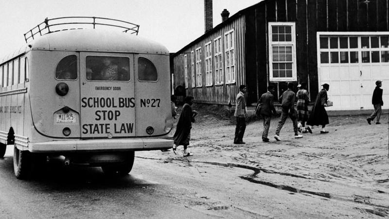 Students walking toward a run down school building on a muddy road