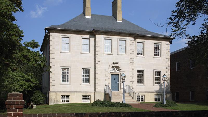 White house with French windows, gray roof, and two chimneys, with a small green lawn surrounding