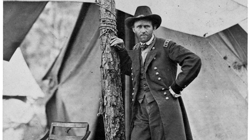 Black and white photo of General Ulysses S. Grant standing next to a tree in a military camp.
