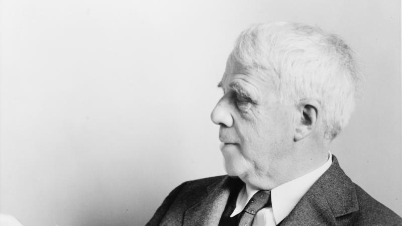 Black and white photo of Robert Frost sitting and reading a manuscript.
