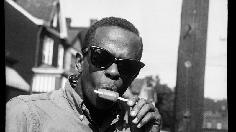 A young, African American man wearing sunglasses and eating a popsicle