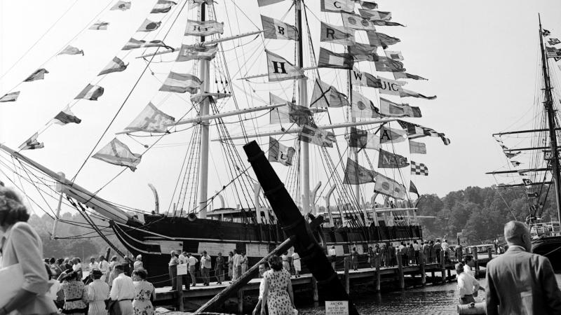 black and white photo of the Charles W Morgan ship, surrounded by people with flags fluttering