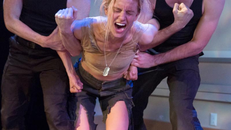 Color photo of two men restraining an angry and distressed woman.