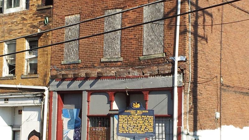 Photo of a run-down three story rowhouse in Pittsburgh, Pennsylvania, with a blue historic signpost in front.