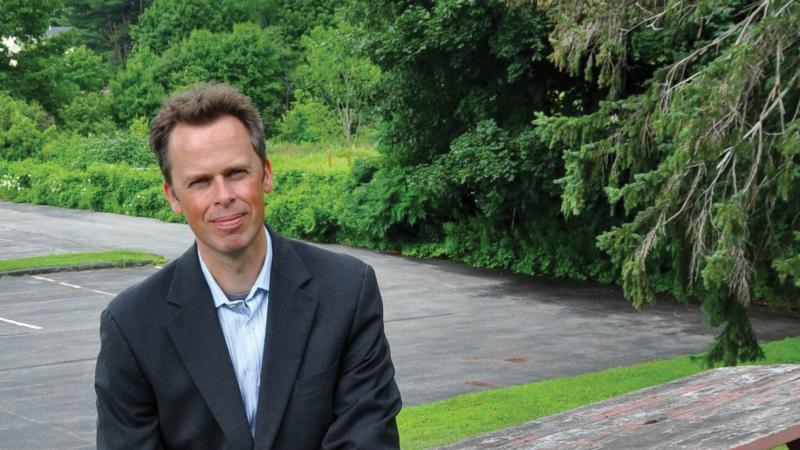 Professional photo of Hayden Andersen sitting at a picnic table with trees in the background.