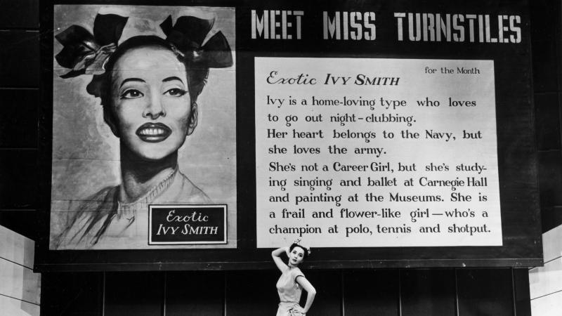 Black and white photo of Sono Osato standing before a large billboard ad for "Miss Turnstiles."