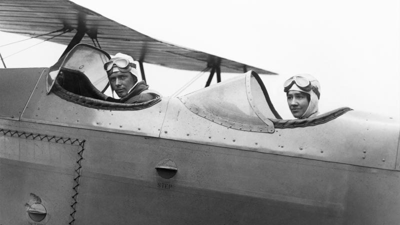 Black and white photo of two individuals sitting in their respective cockpit seats in a plane.