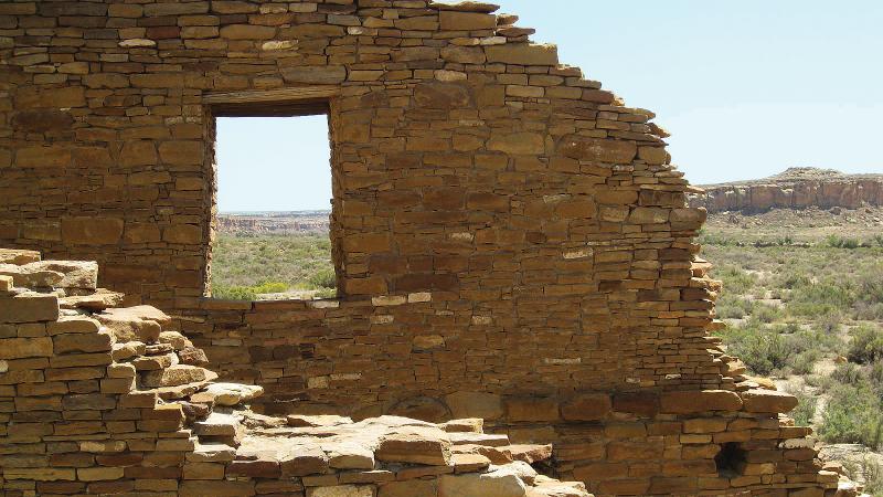 Color photo of a demolished brick facade facing an open field. 