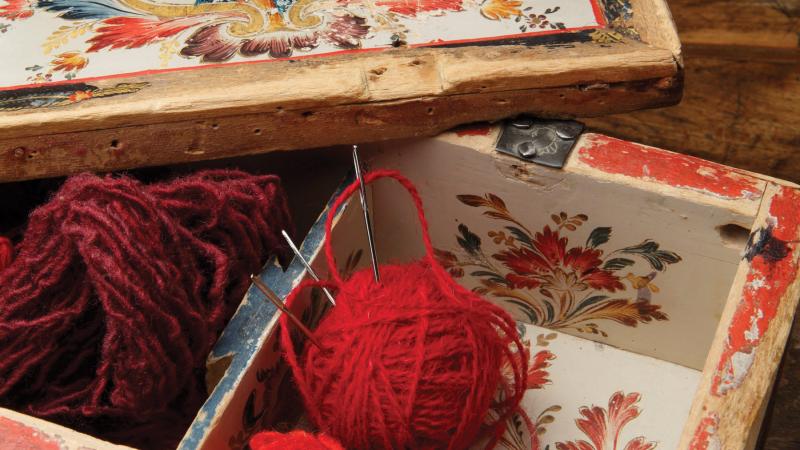 Wooden sewing box painted with red flowers and a portrait of a man, containing several balls of red wool yarn