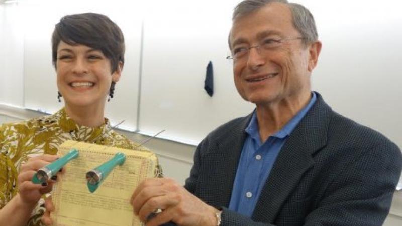 A woman (left) and a man (right) dressed in business casual attire hold a yellow McBee punch card up to the camera.