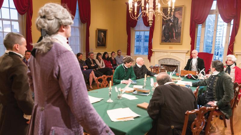 Photograph of men in period clothing and wigs at a table