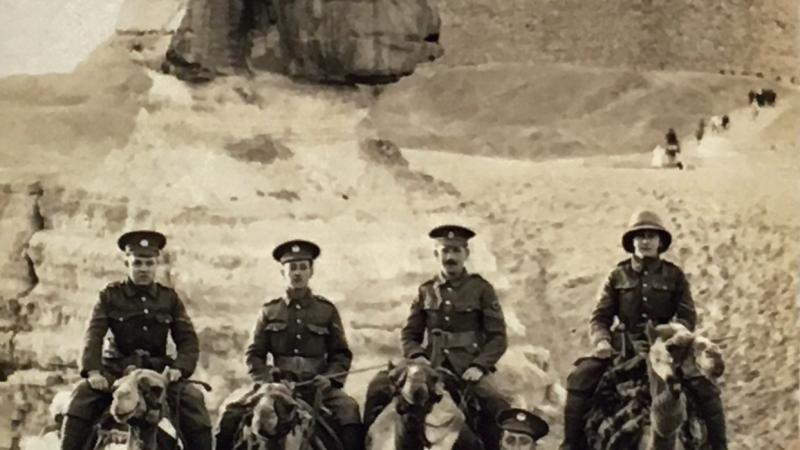 Sepia-colored photo of mounted soldiers posing before the pyramids of Egypt.