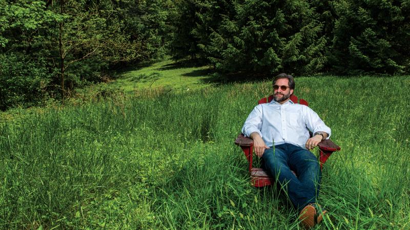 Photograph of man sitting in adirondack chair in tall grass